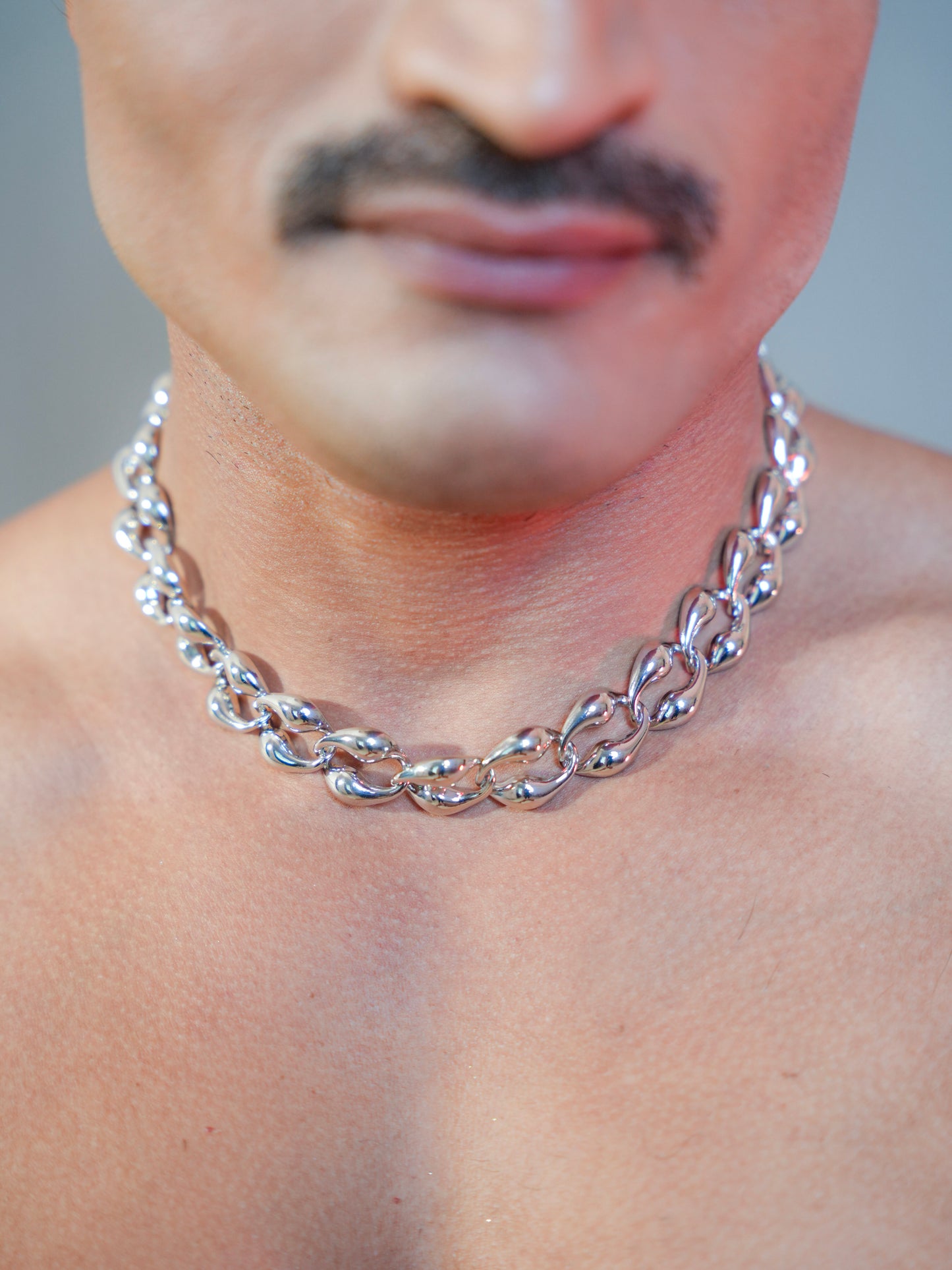 Close-up of a person wearing a silver chain necklace with a blurred background