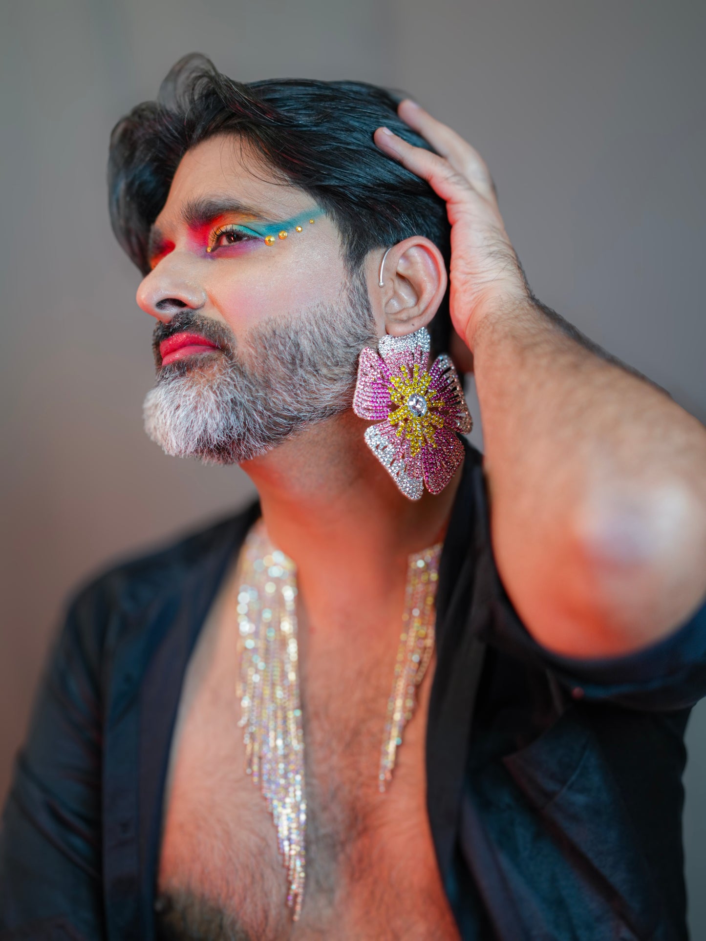 Person with colorful makeup and jewelry, wearing a black outfit.