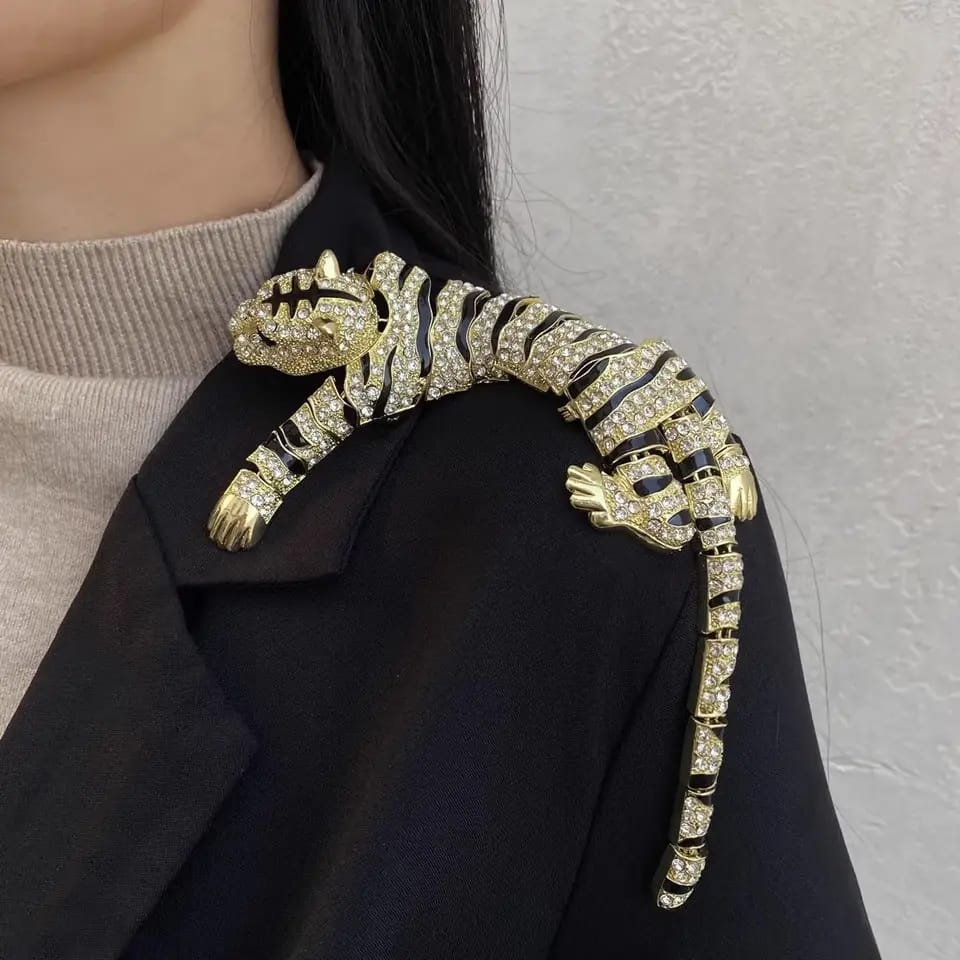Gold tiger brooch on a black coat against a neutral background
