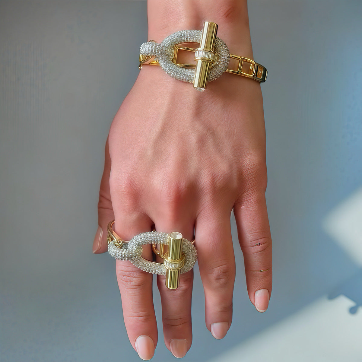 Close-up of hand wearing gold and silver rope-textured bracelet and ring with cylindrical clasp – bold, modern jewelry design.