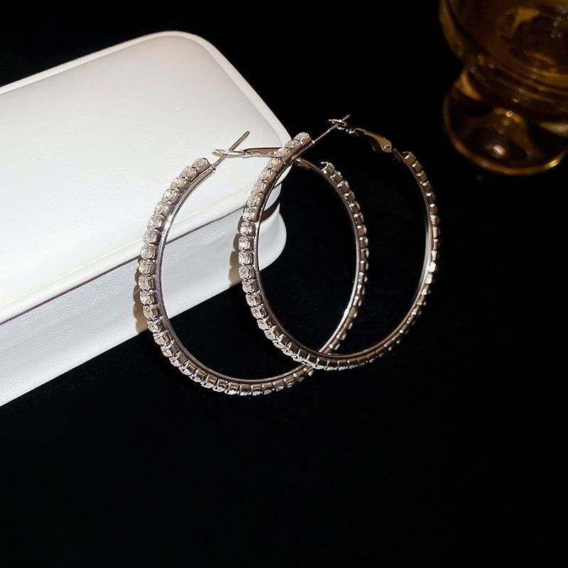 Pair of silver hoop earrings on a dark surface with a white box in the background.
