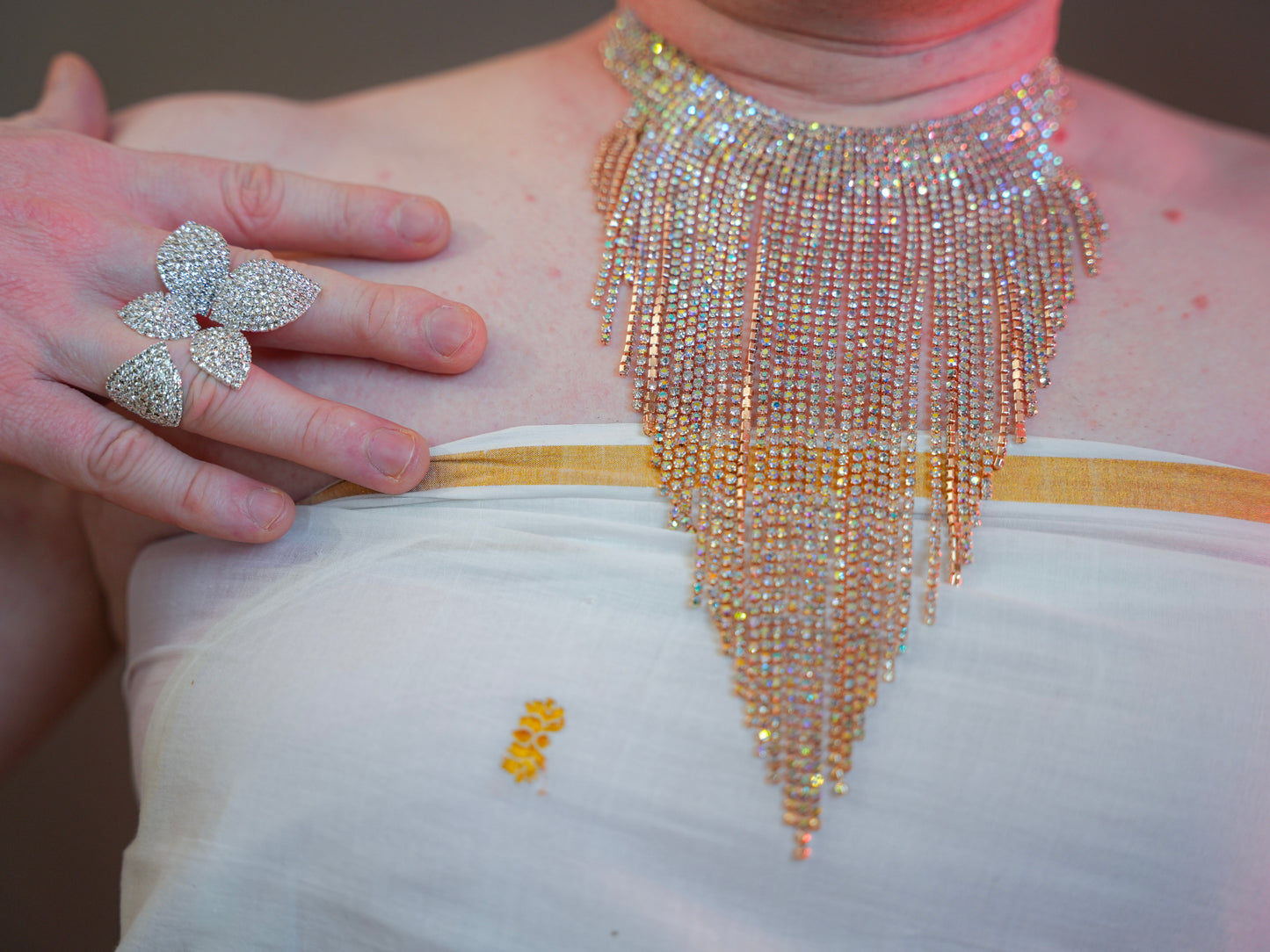 Luxurious tassel necklace displayed on a black mannequin bust. The necklace features cascading rows of sparkling rhinestones in a triangular pattern, set in gold-toned metal, with a glamorous blurred light background.
Want to add a tribute line or nickname from your glossary to make Tarra part of the #BondedByPride collection? I’d love to help you weave that in with heart.