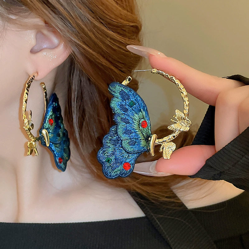 Close-up of a person wearing large hoop earrings with butterfly designs.