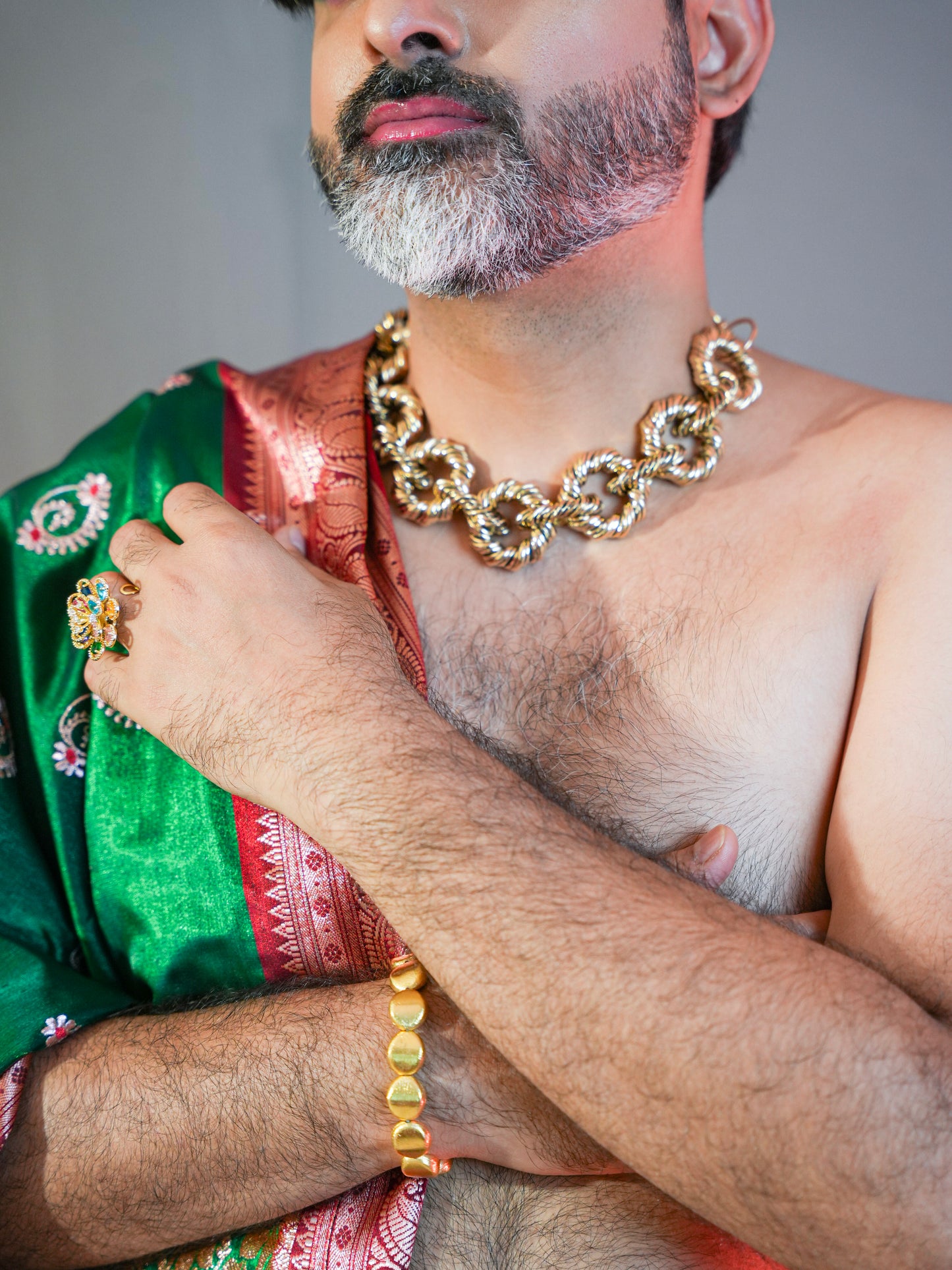 Man wearing a gold chain necklace and green traditional garment with a plain background