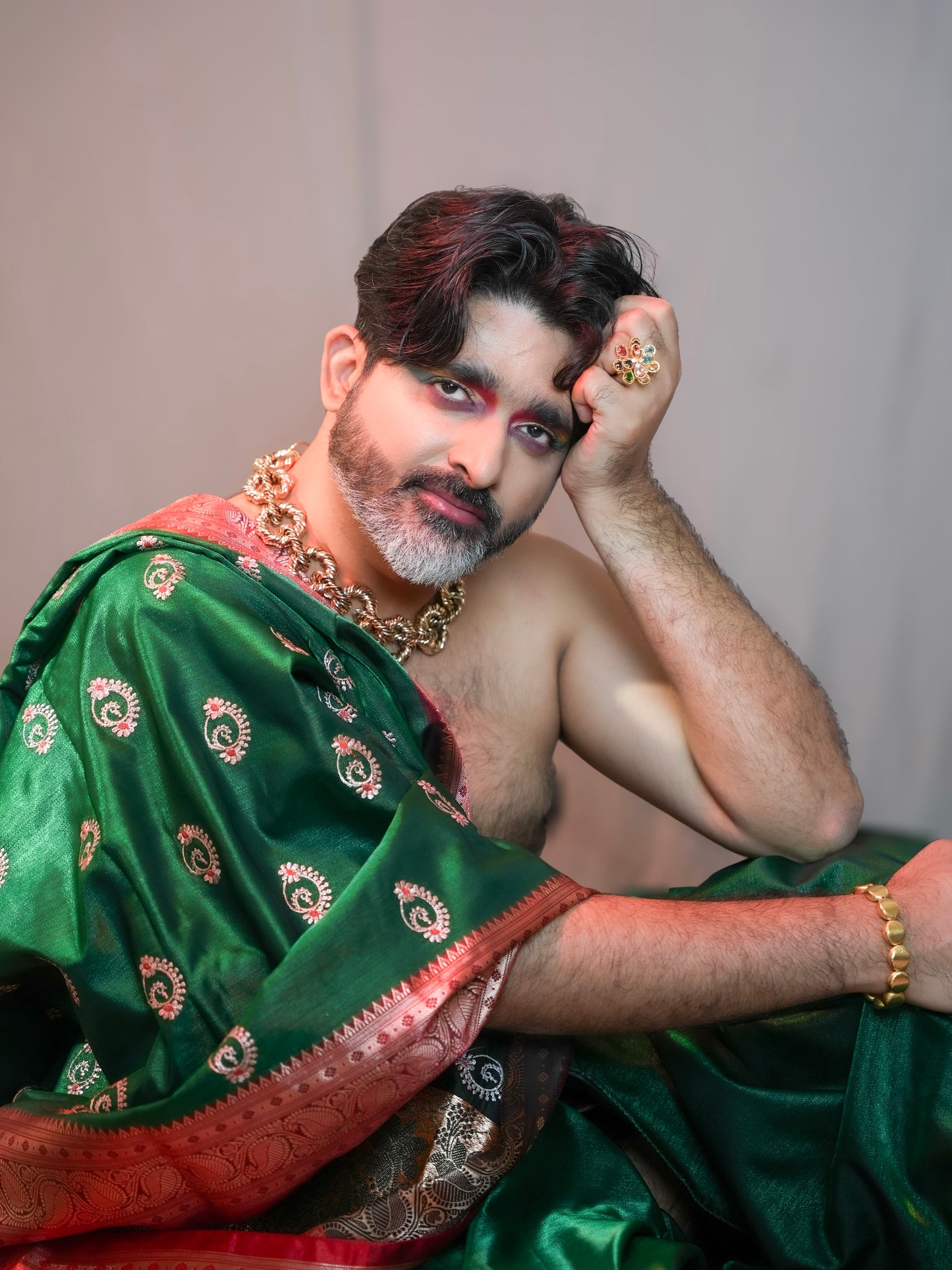 Person wearing a green saree with gold jewelry against a plain background