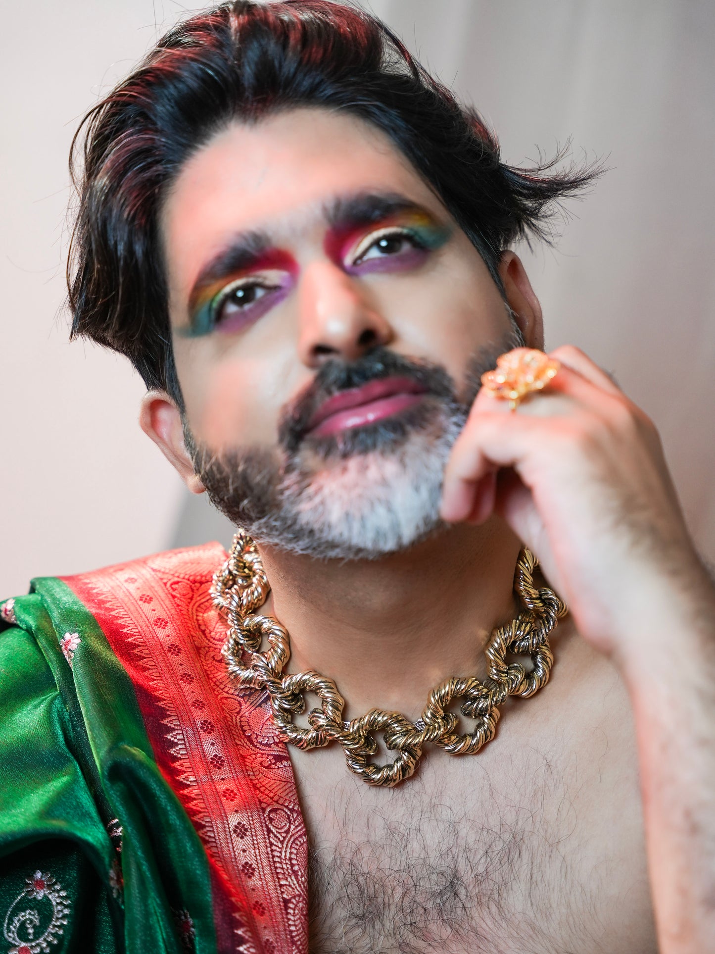 Person wearing a green and red traditional outfit with a gold chain, against a neutral background.