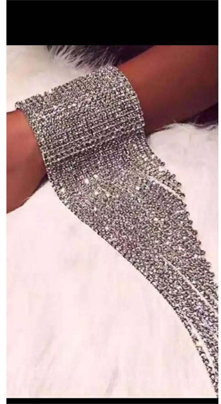 Close-up of wrist wearing the Hilyn Bracelet—an ornate rhinestone cuff with long, dangling strands, styled against a soft white furry background.