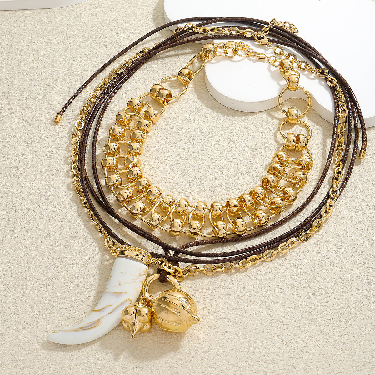 Balor Gold Chain Set displayed—chunky gold chain bracelet and layered necklaces with brown cord, gold links, a white tusk charm, and a gold spherical pendant. its a three layer chain set