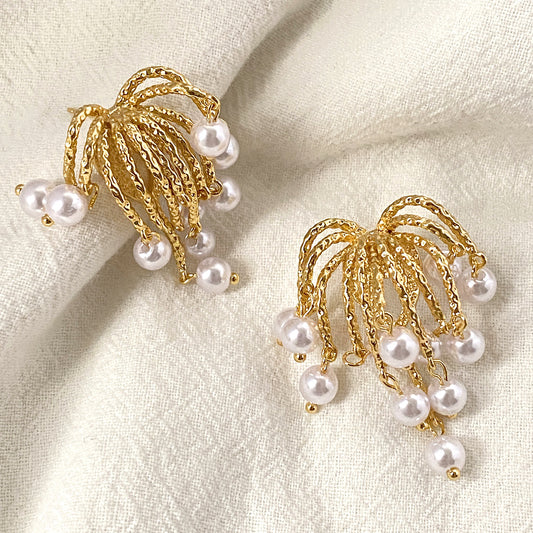 Luxurious cascading pearl earrings with textured gold arches and dangling freshwater pearls, displayed on a white fabric backdrop.