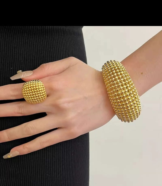 Close-up of hand wearing gold textured ring and matching bracelet with raised dot pattern – bold statement jewelry against black ribbed fabric.