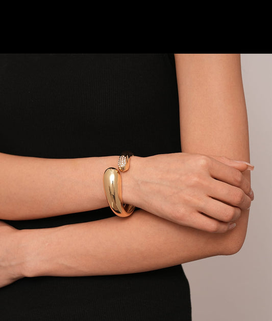 Close-up of crossed arms wearing a gold bangle and crystal-accented bracelet – statement wrist jewelry for elegant layering.