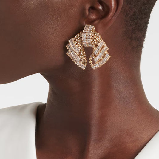 Close-up of a person wearing gold earrings with a neutral background