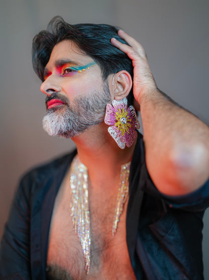 Person with colorful makeup and jewelry, wearing a black outfit.
