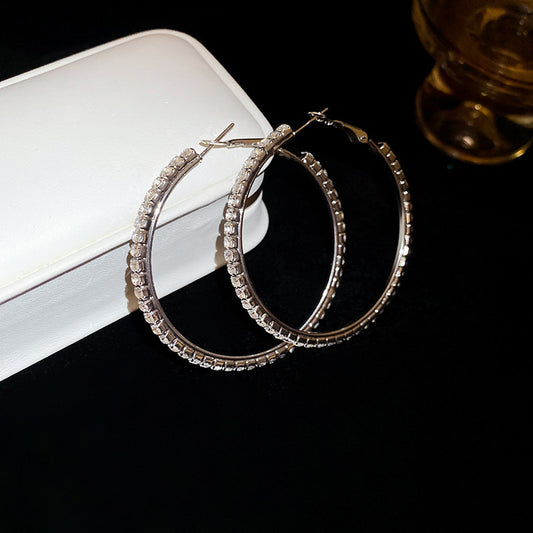 Pair of silver hoop earrings on a dark surface with a white box in the background.