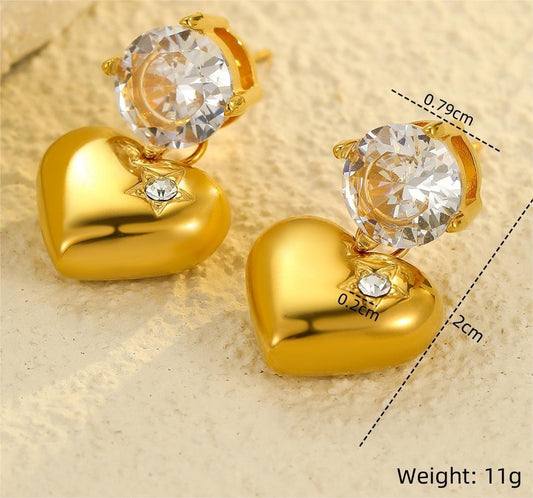 Gold heart-shaped earrings with round crystal tops and embedded gem detail – lightweight statement studs displayed on textured surface with measurements.