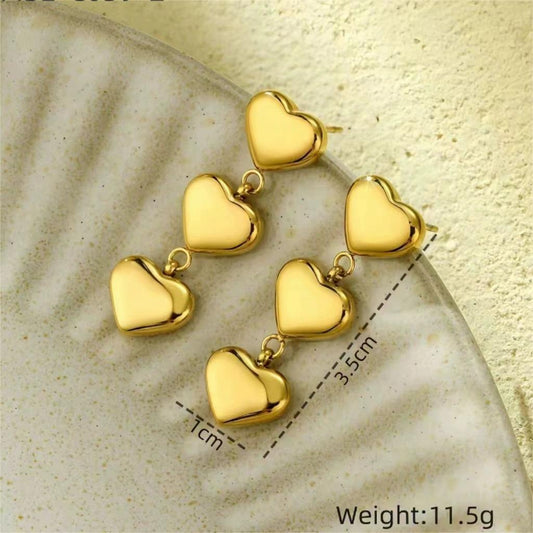 Six gold heart-shaped charms arranged in pairs, each measuring 1 cm × 3.5 cm, displayed on a textured surface.
