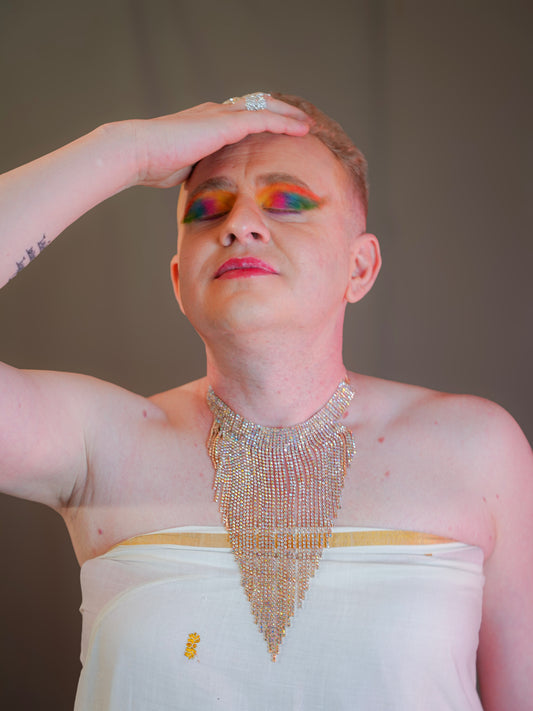 Person with colorful makeup and a sparkling necklace against a neutral background
