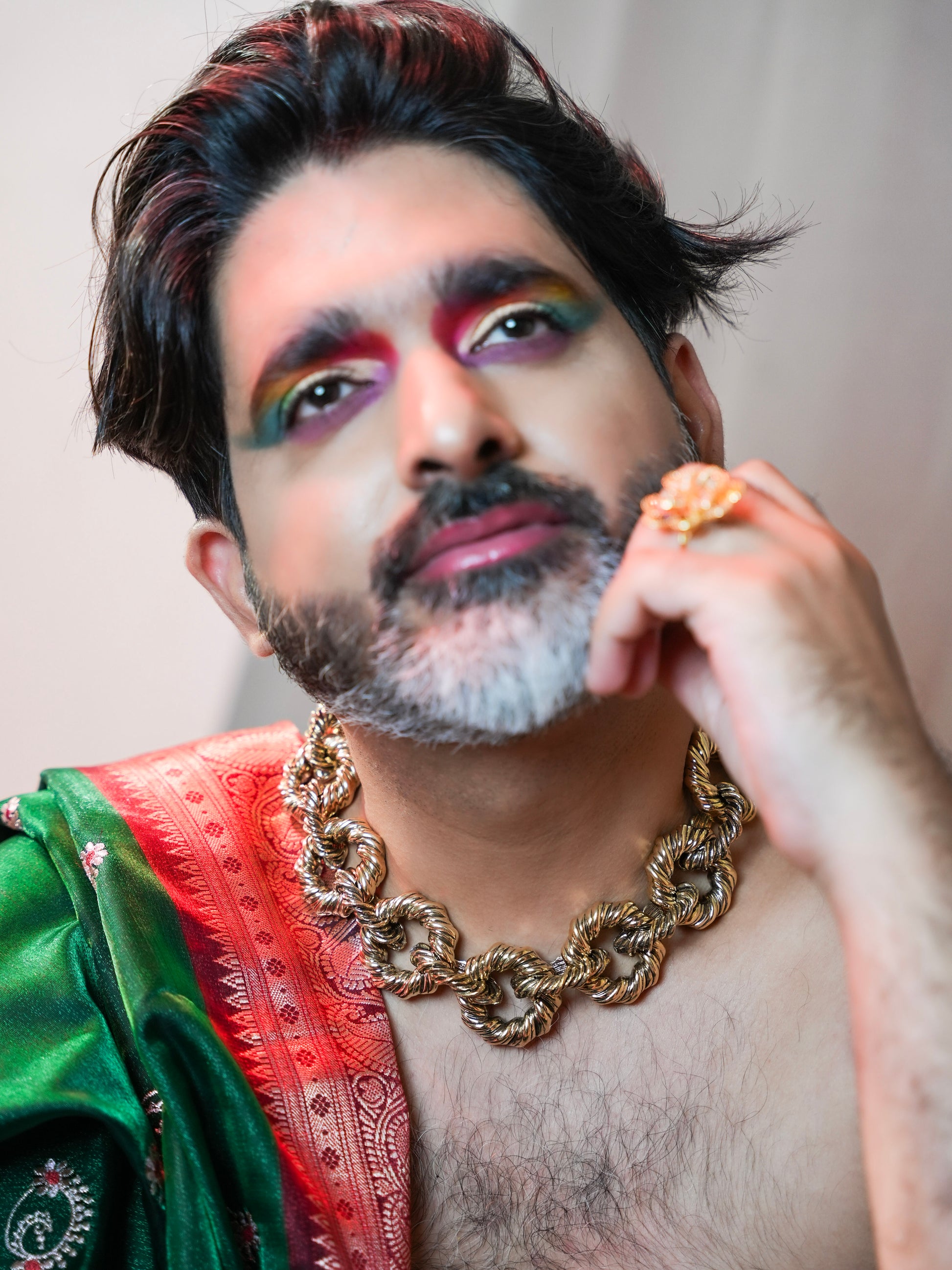 Person wearing a green and red traditional outfit with a gold chain, against a neutral background.