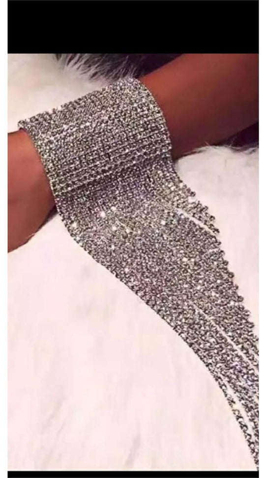 Close-up of wrist wearing the Hilyn Bracelet—an ornate rhinestone cuff with long, dangling strands, styled against a soft white furry background.